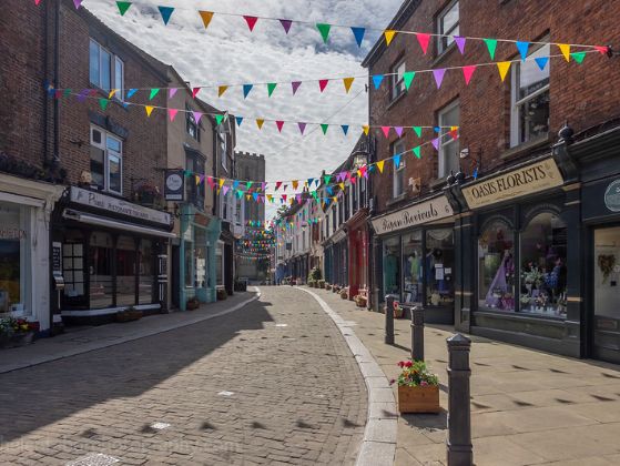 image of cobbled street with shops either side and multicoloured buntin zigzagging from building to building